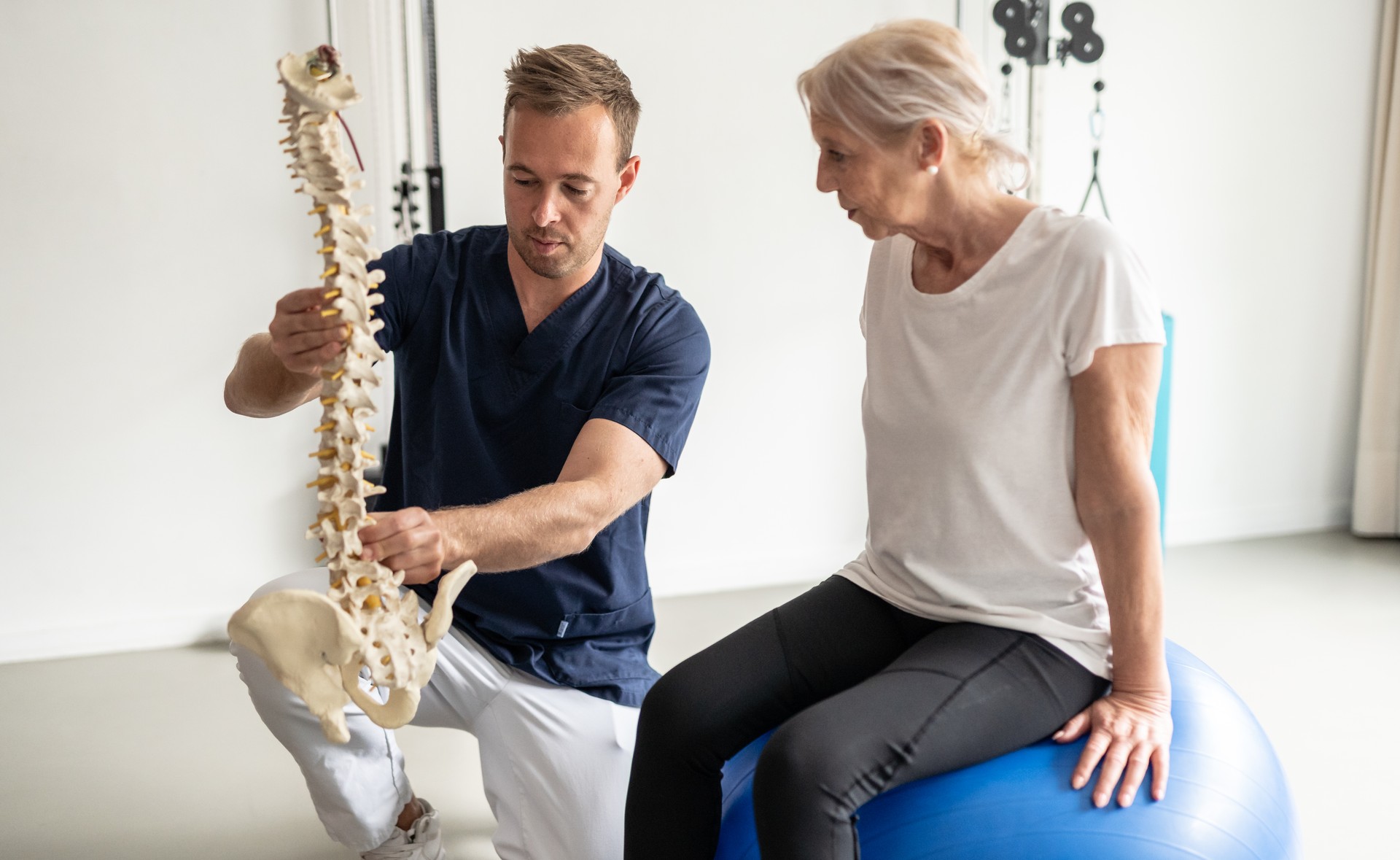 Professional doctor showing elderly patient through therapeutic exercises on a medicine ball.